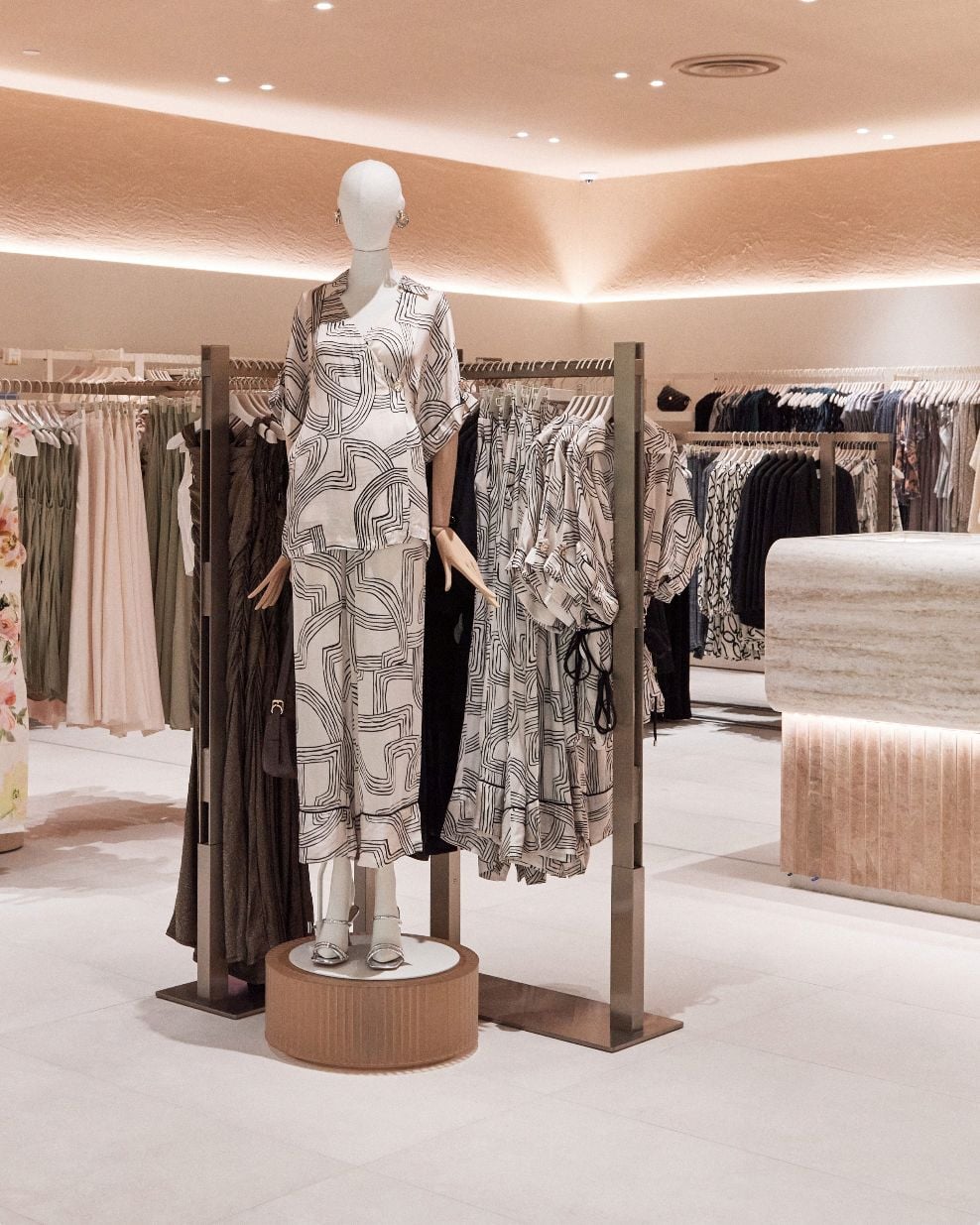 Store interior — printed outfit on a plinth beside travertine